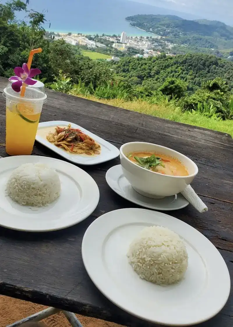 Thai dishes, rice and an iced drink on a wooden table above the coast