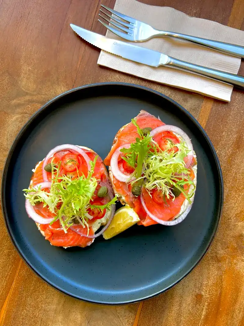 Two bagel halves topped with smoked salmon, onion and frisée on a dark plate