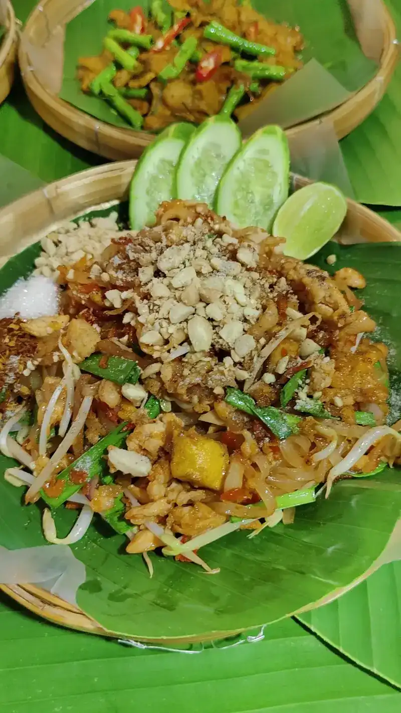 Pad thai with crushed peanuts, bean sprouts, cucumber and lime on banana leaf in a woven basket