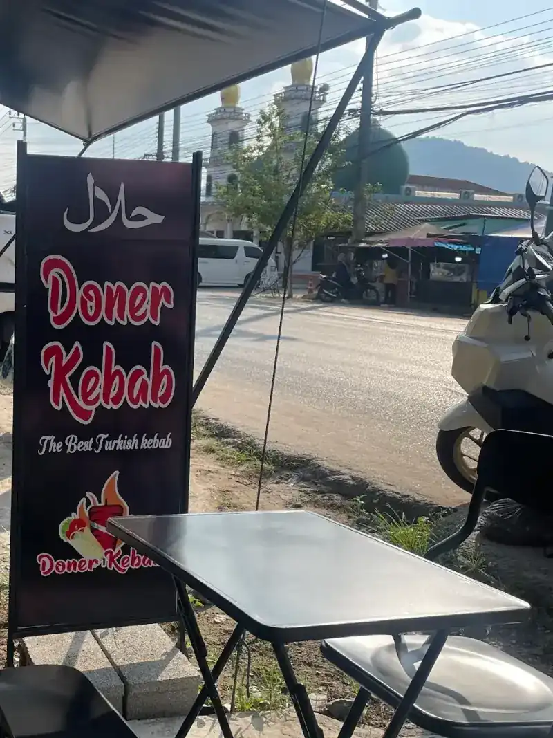 The halal doner kebab banner by the outdoor tables, with a mosque across the road