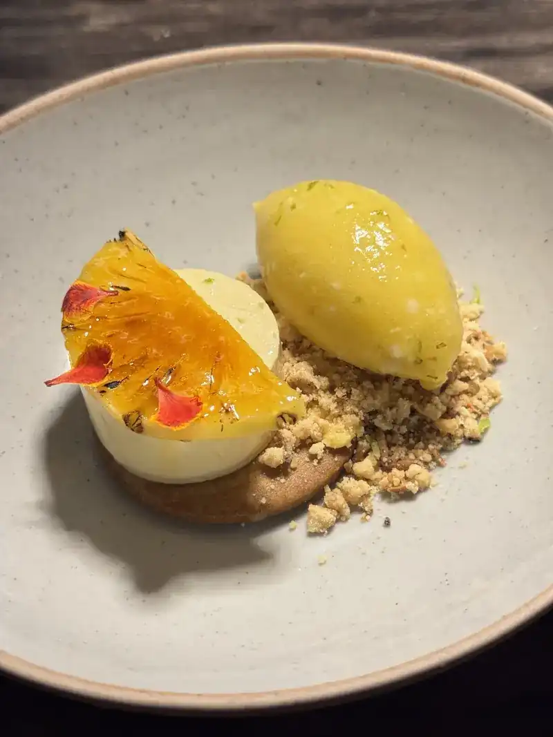 A dessert with a glazed citrus slice, a yellow scoop and crumble