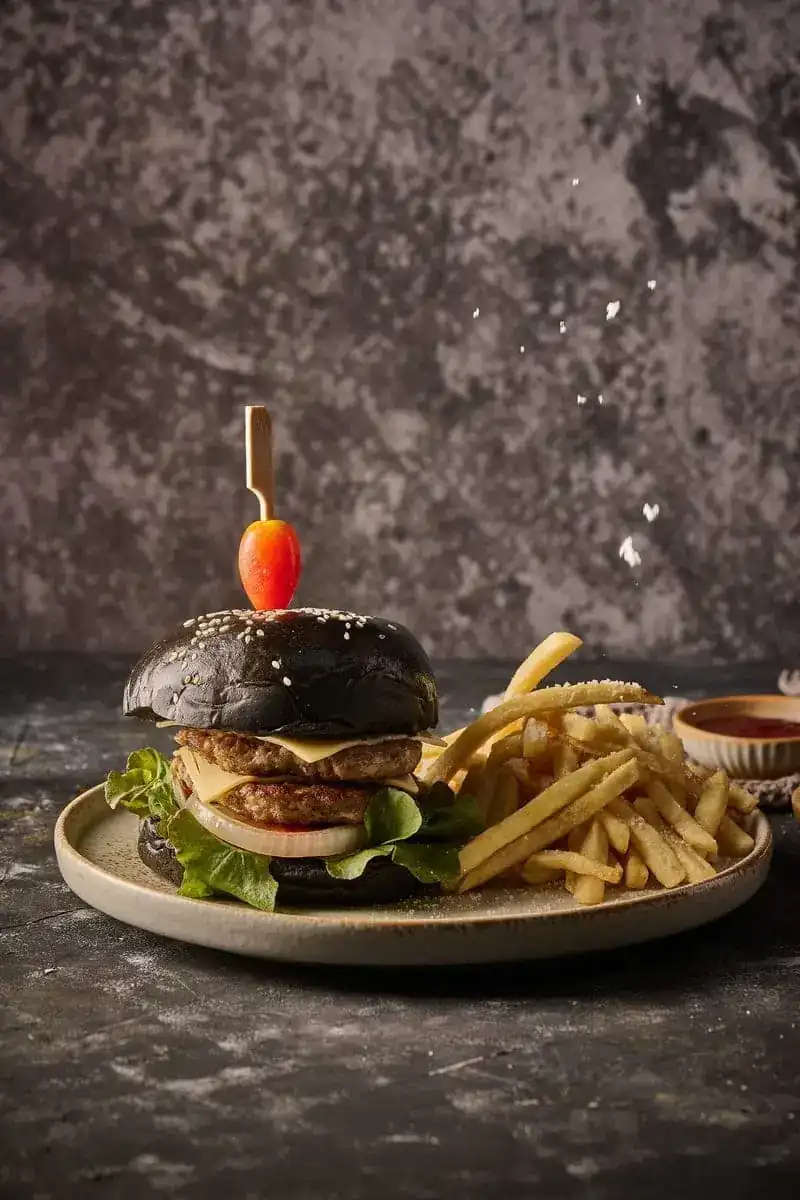 A pork burger in a black charcoal bun with fries