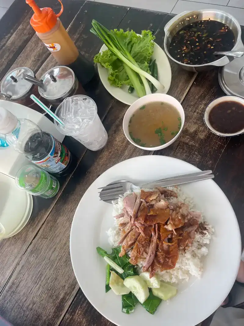 A table with duck on rice, a bowl of clear soup, dipping sauces and a plate of lettuce and spring onion