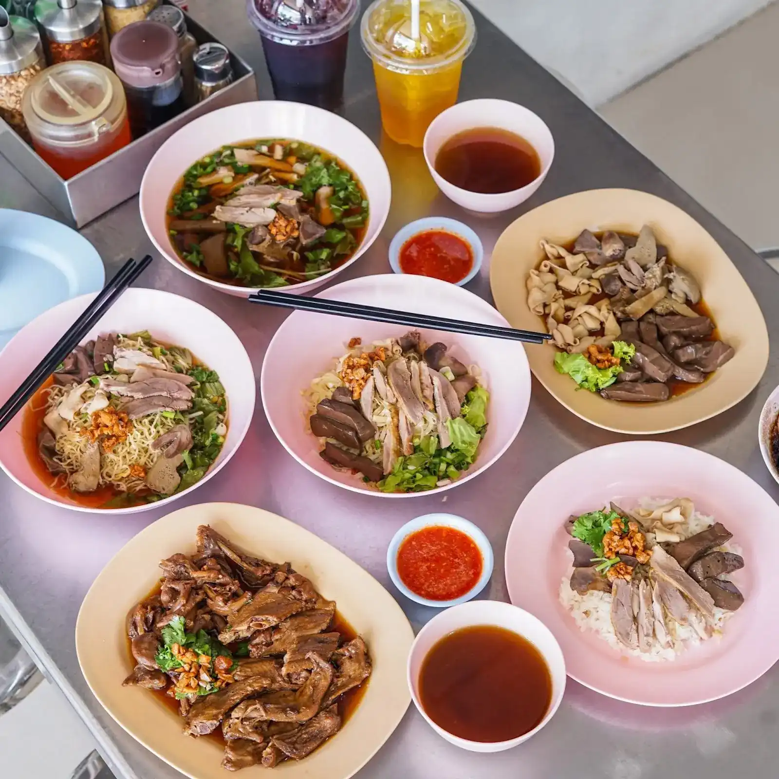 A table of Kitti dishes: duck noodle soup, dry duck noodles, braised offal, stewed duck and duck on rice, with bowls of broth and chilli sauce / โต๊ะเต็มไปด้วยเมนูกิตติ: ก๋วยเตี๋ยวเป็ดน้ำ ก๋วยเตี๋ยวแห้ง เครื่องในพะโล้ เป็ดตุ๋น และข้าวหน้าเป็ด พร้อมน้ำซุปและน้ำจิ้ม