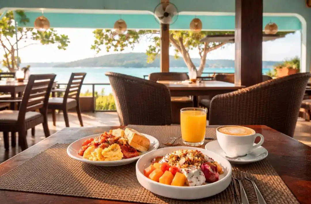 Brunch plates, juice and coffee on a table with the sea and hills behind