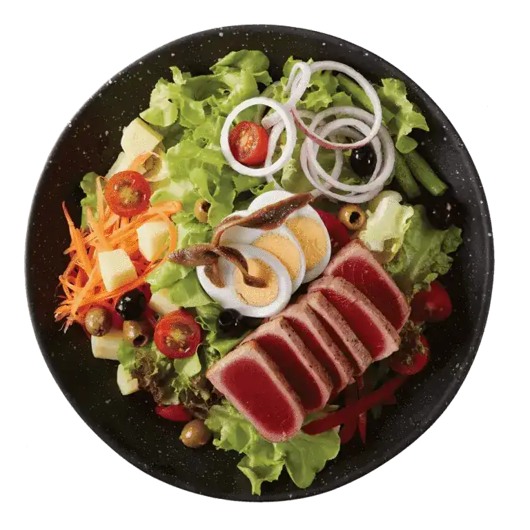 Seared tuna salad with boiled egg, anchovy, olives and greens on a black plate