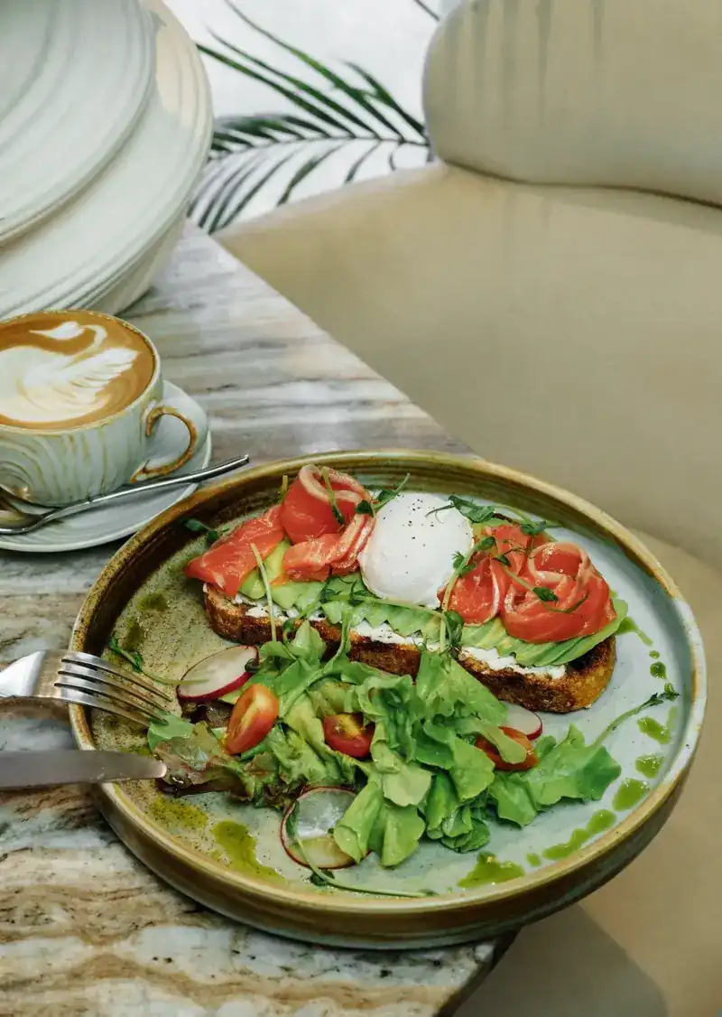 Salmon toast with a poached egg, on a marble table beside a coffee