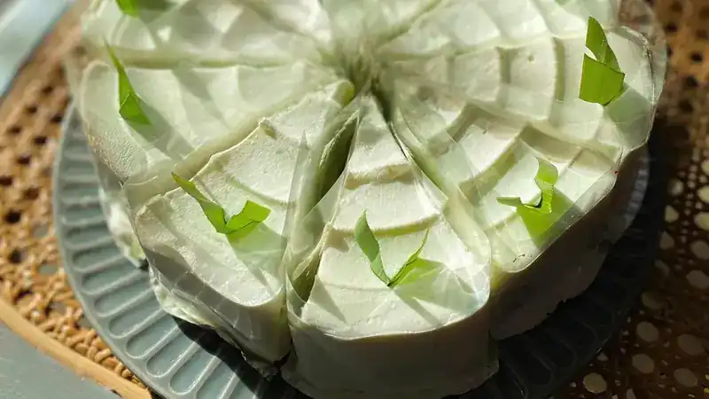 A pale green cream cake cut into wrapped slices on a grey plate
