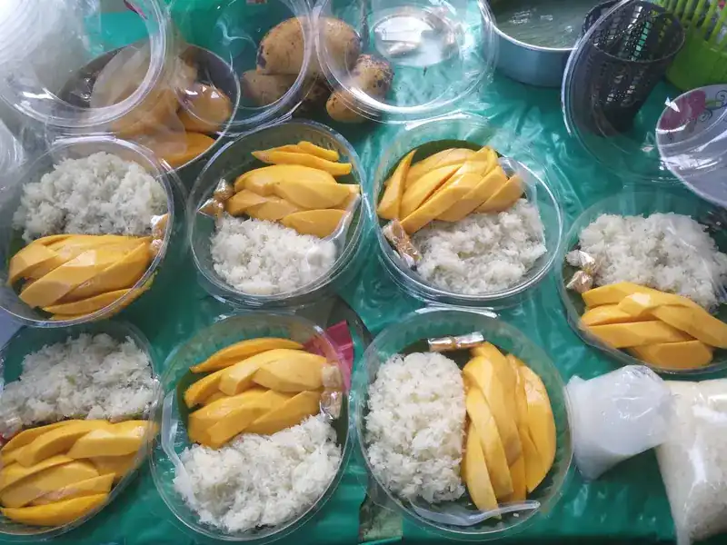 Clear bowls of sticky rice and sliced mango laid out on the stall's green table