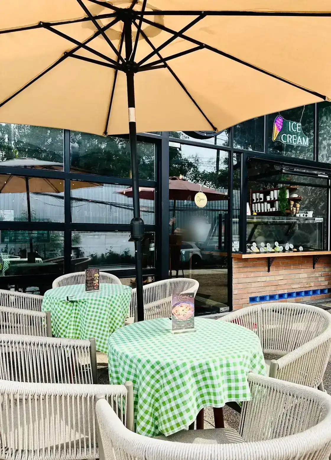 The terrace: green-checked tables and rope chairs under a cream umbrella, with the ice cream window counter behind