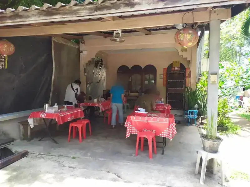 The porch of the house with red checked tablecloths, red plastic stools and paper lanterns, guests eating at the back