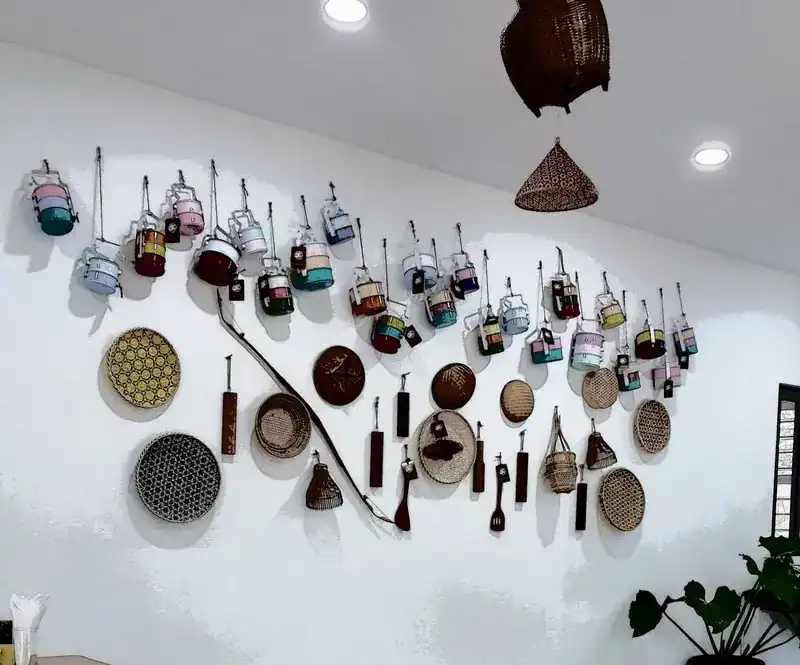 A white wall hung with colourful enamel pinto food carriers and woven baskets