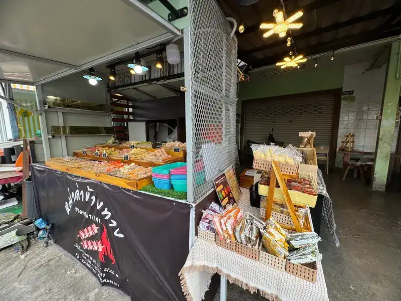 The stall under hanging lamps, trays of skewers in front and a snack rack beside it