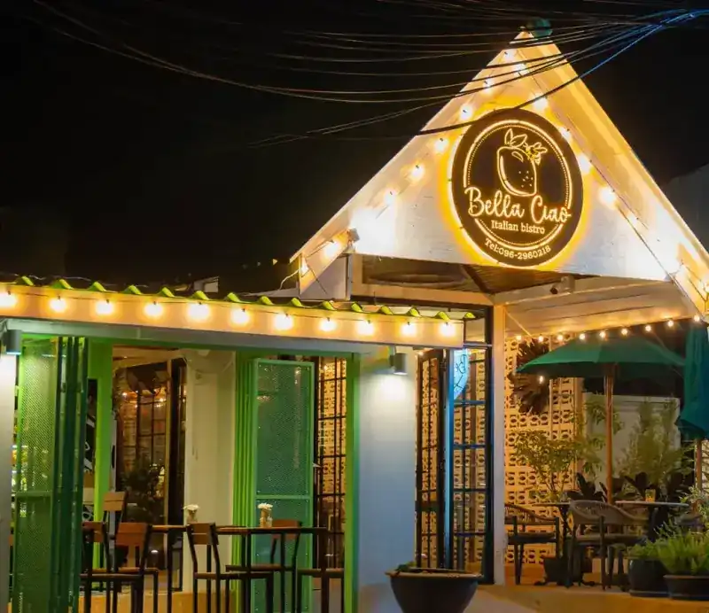 The white gabled front of the bistro at night, lit with string lights