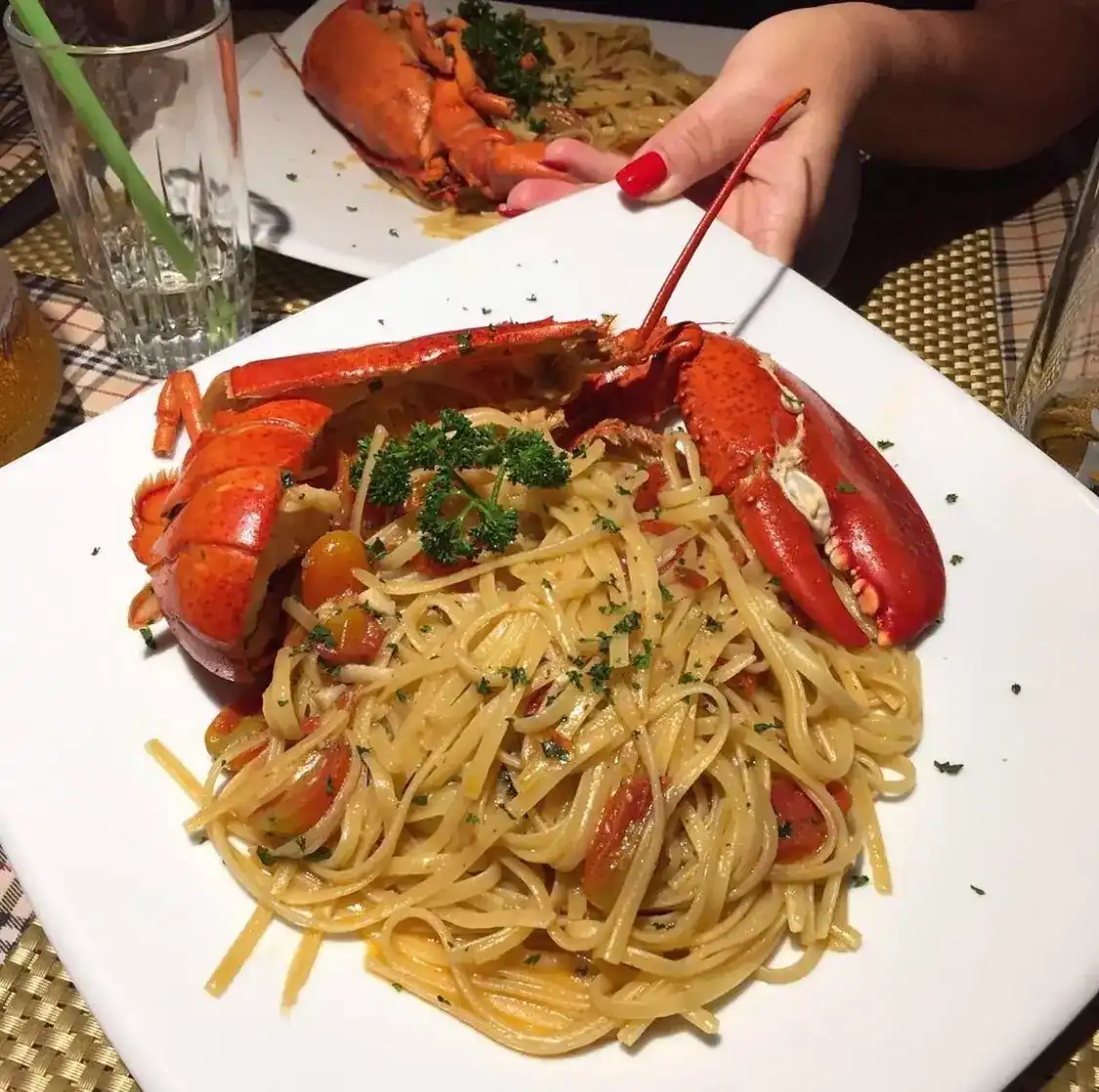 Linguine with a whole lobster, cherry tomatoes and parsley on a white plate