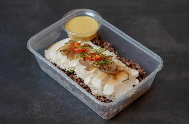 Sliced chicken breast over brown rice with a pot of panang sauce