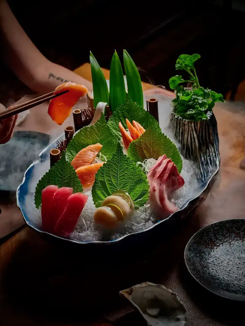 Sashimi on ice with shiso leaves, a hand lifting a slice with chopsticks / ซาชิมิบนน้ำแข็งกับใบชิโสะ มือคีบปลาด้วยตะเกียบ