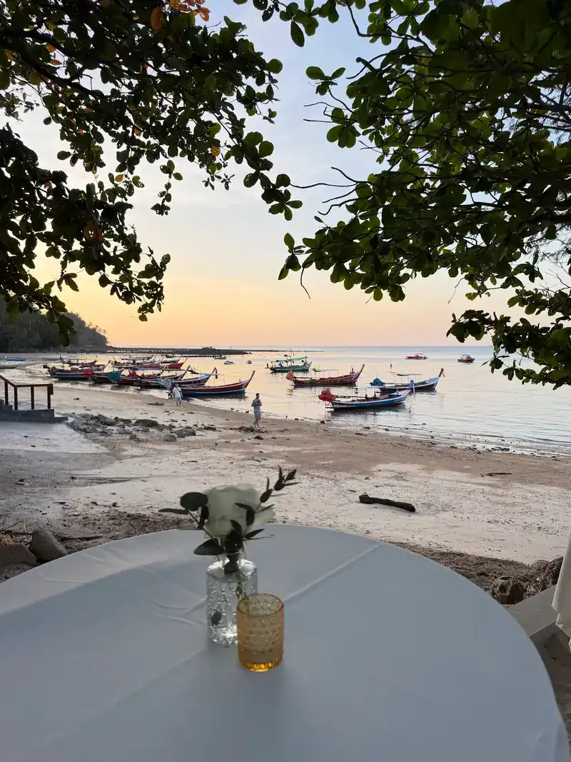 A table set with a small vase, looking out at boats in the bay at dusk