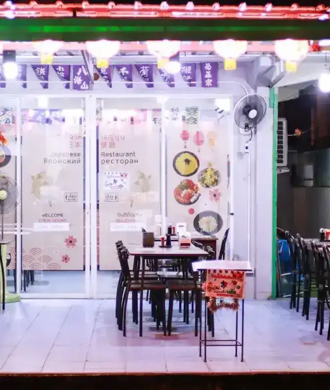 Kin Sushi's front terrace at night: paper lanterns under the roof, purple banners over the glass doors, and empty tables