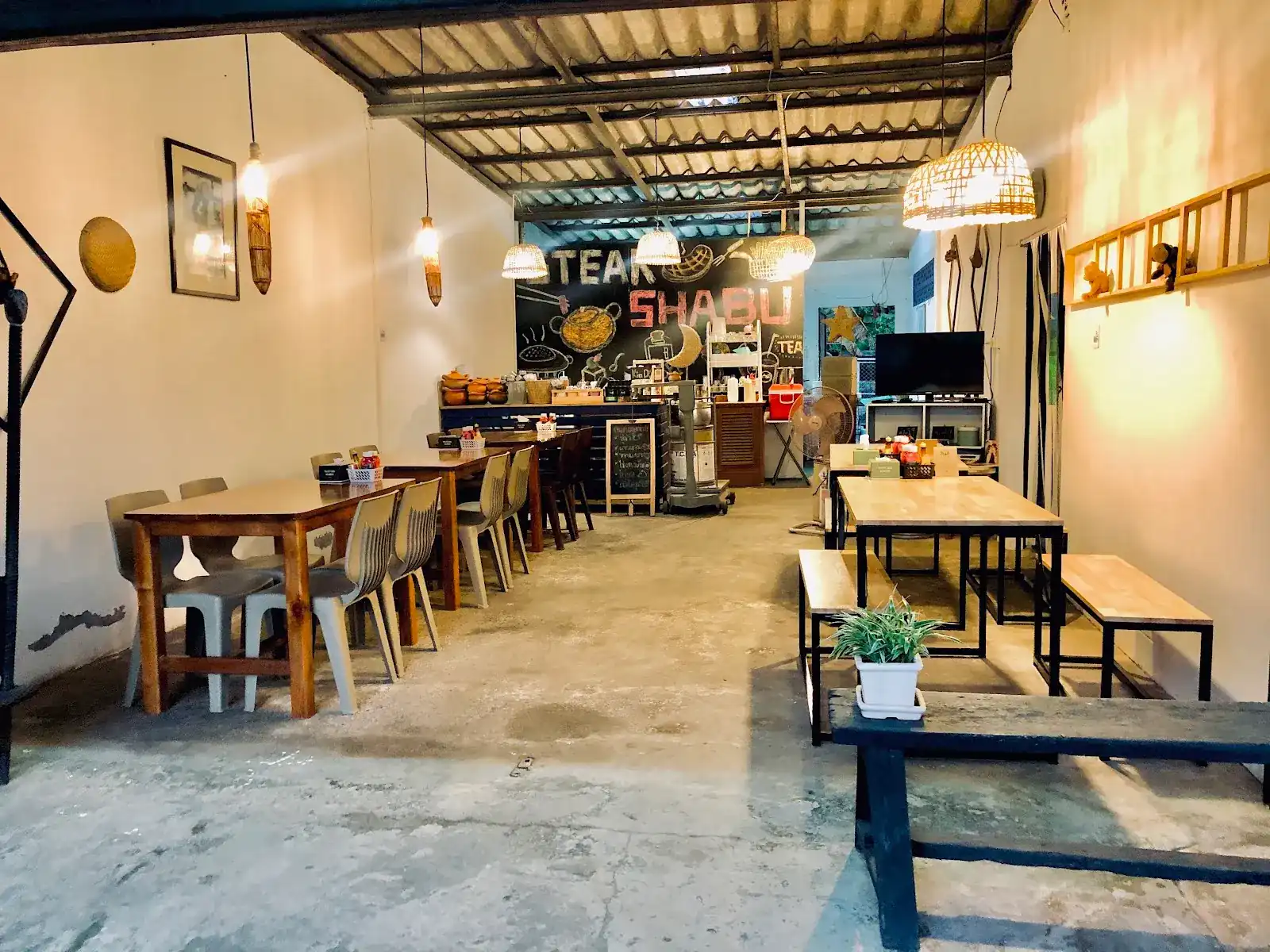 Inside Kin Dee Bang Rong: wooden tables and benches on a concrete floor, rattan lamps, and a chalk wall reading steak and shabu at the back / ภายในร้านกินดีบางโรง โต๊ะไม้และม้านั่งบนพื้นปูน โคมไฟหวาย และผนังกระดานดำเขียนว่าสเต๊กและชาบูที่ด้านหลัง