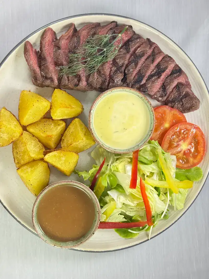 Sliced grilled steak with roast potatoes, salad, tomato and two sauces