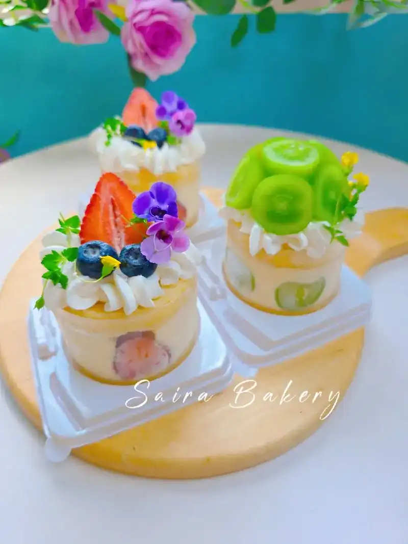Small round cakes topped with cream, strawberry, blueberries and violet flowers, one with green grapes