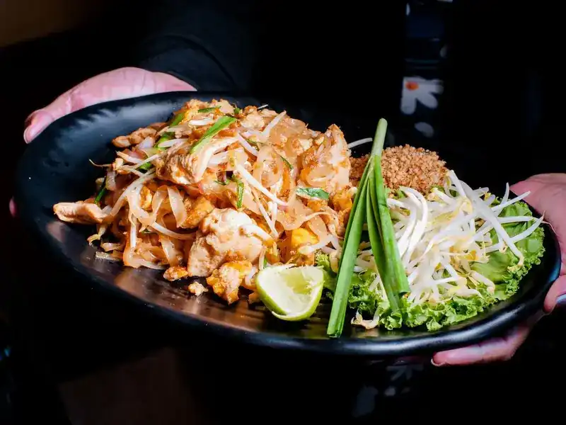 A plate of stir-fried rice noodles with bean sprouts, crushed peanuts and lime