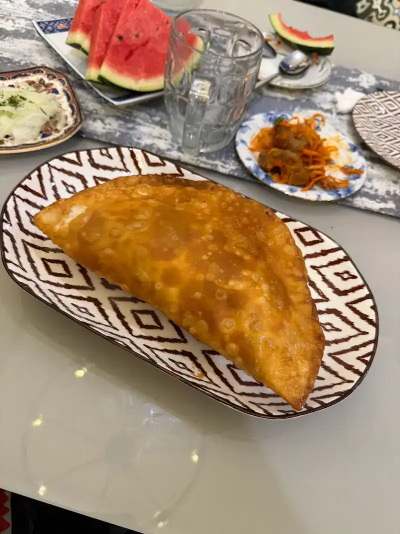A golden fried pastry folded into a half-moon on a patterned plate