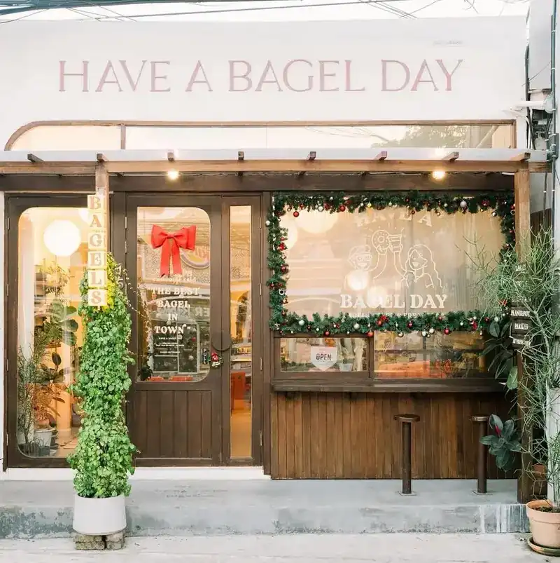 The shop front: a white sign reading Have a Bagel Day above a wooden front, a glass door and plants