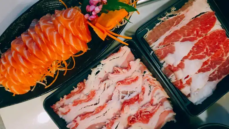 Salmon sashimi beside trays of sliced pork and beef