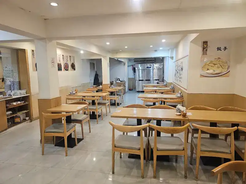 Long dining room with wooden chairs, a dumpling poster and the kitchen at the back