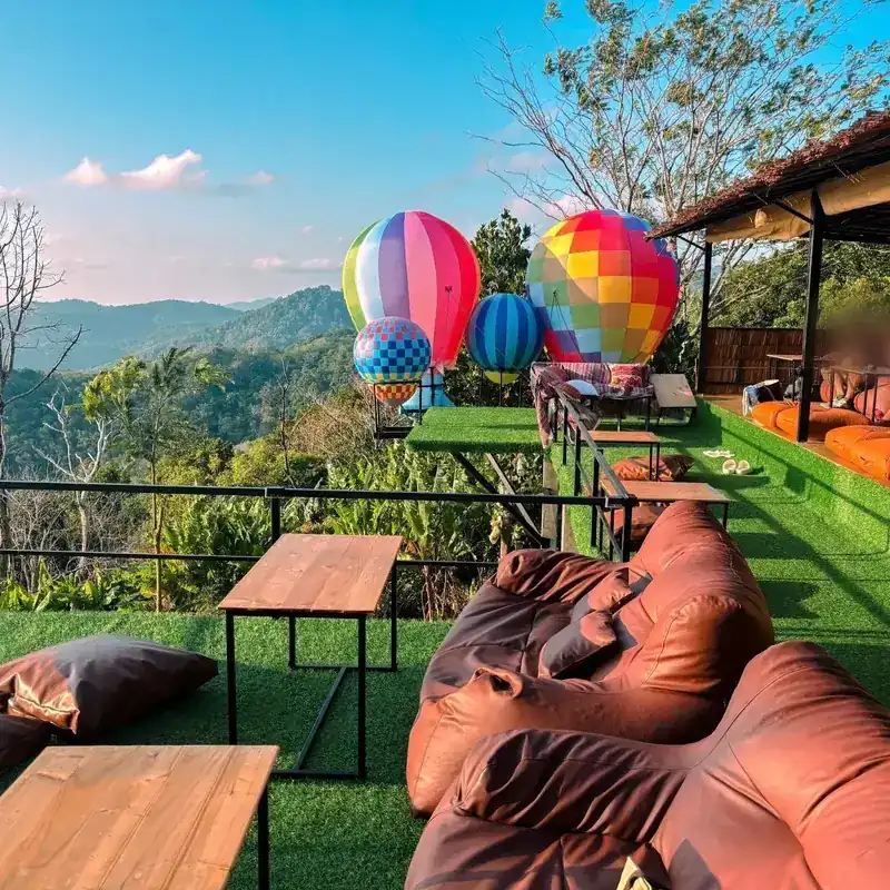 Leather bean bags and tables on the grass terrace, balloons and green hills behind