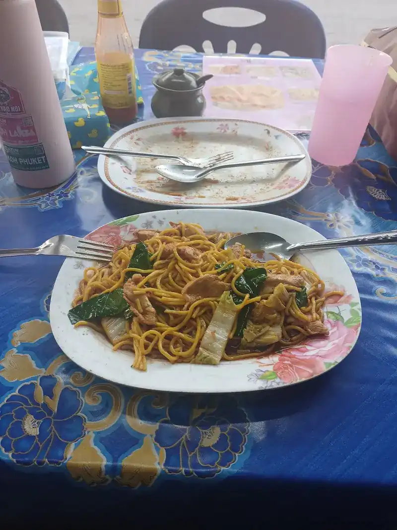 A plate of fried yellow noodles with greens on a blue tablecloth