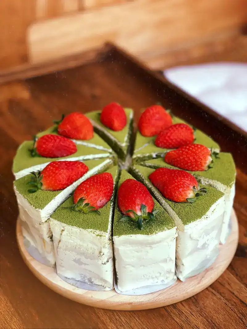A whole matcha cake cut into slices, each topped with a strawberry