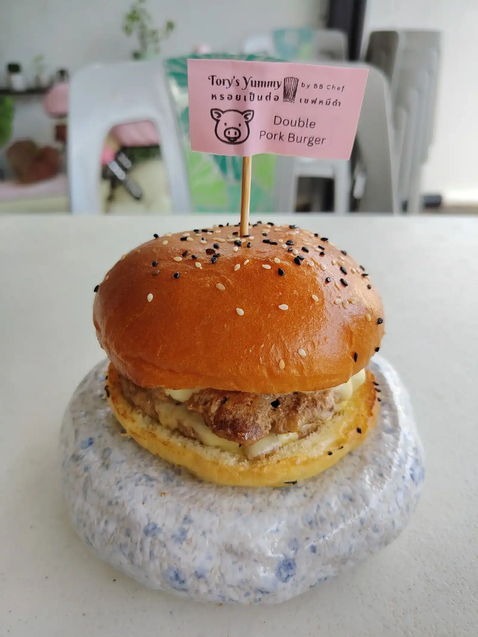 A Double Pork Burger on a speckled stand, wearing its pink Tory's Yummy name flag