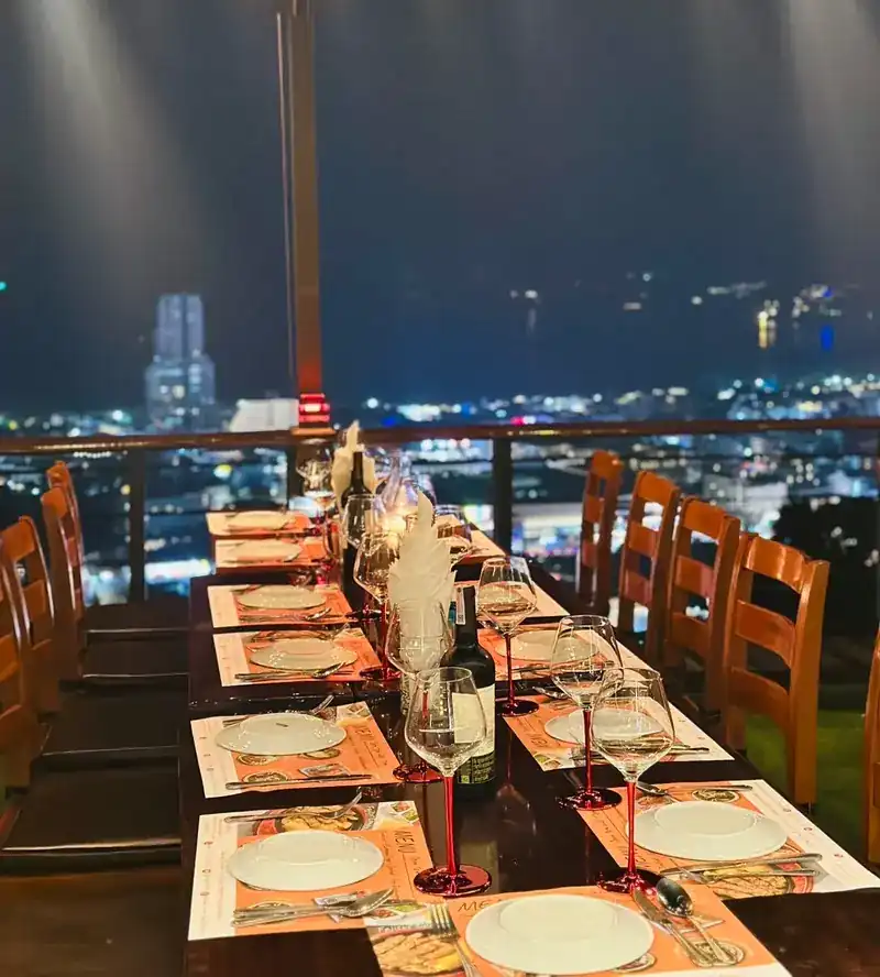 A long table set for dinner on the terrace at night, the lights of Patong behind the railing