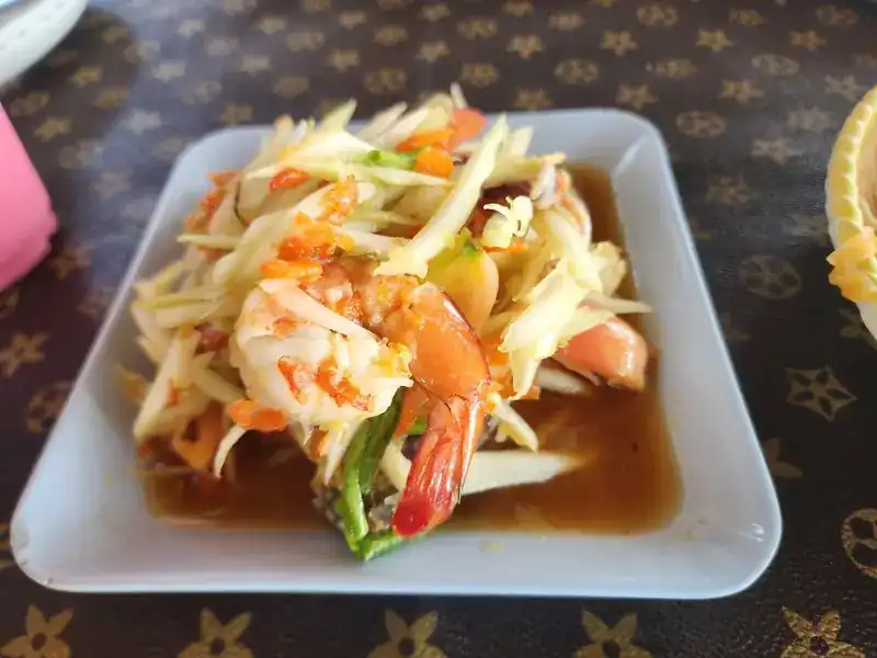 Green papaya salad with prawns and tomato on a white plate