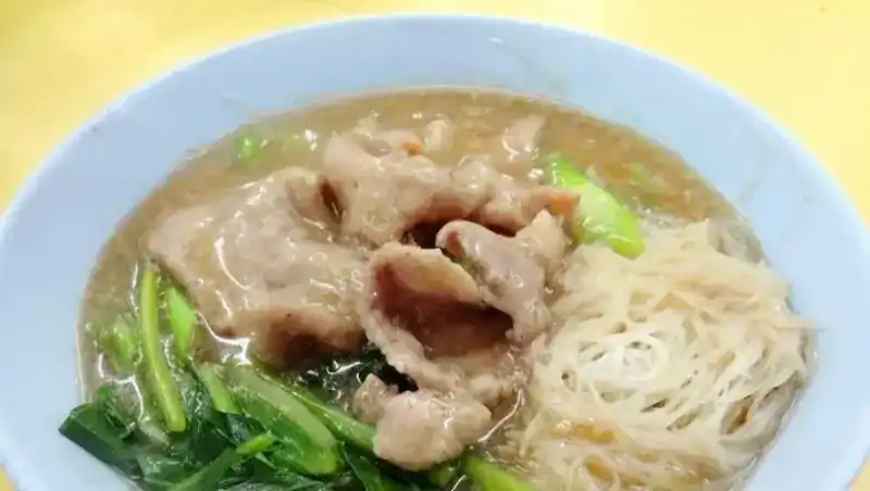 A bowl of noodle soup with thin rice noodles and Chinese kale