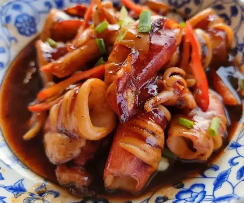 Squid in a dark, glossy sweet sauce with chilli and spring onion, in a blue and white bowl