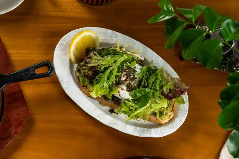 Avocado toast with a poached egg, salad leaves, seeds and a wedge of lemon