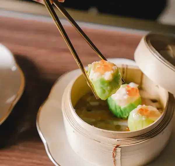 Dim sum lifted from a bamboo steamer with chopsticks