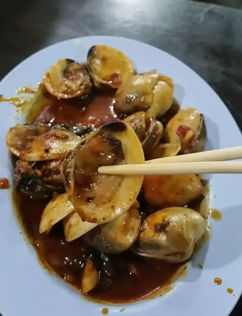 Clams stir-fried in a dark chilli sauce, picked up with chopsticks