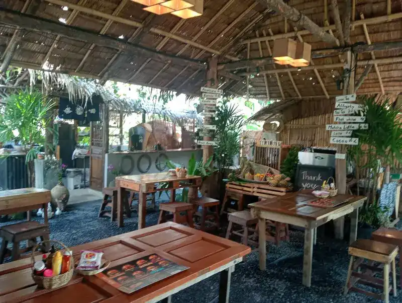 Inside the thatched dining room: wooden tables, plants and painted wooden signposts