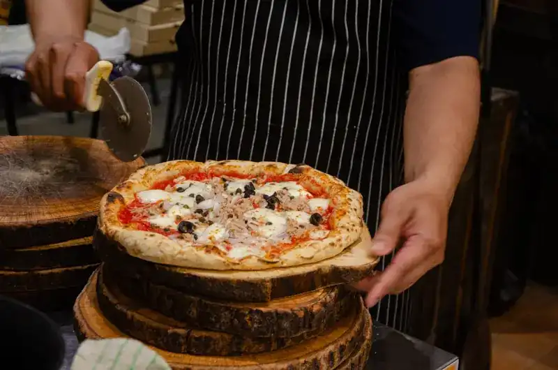 A pizza just out of the oven, held on a wooden board beside a pizza cutter