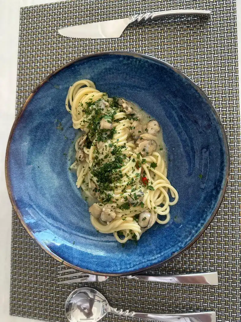 Spaghetti in a light sauce with chopped parsley in a deep blue bowl, with knife, fork and spoon