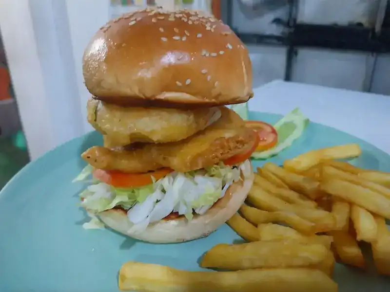 A tall burger with crispy fried fillets, lettuce and tomato, served with chips
