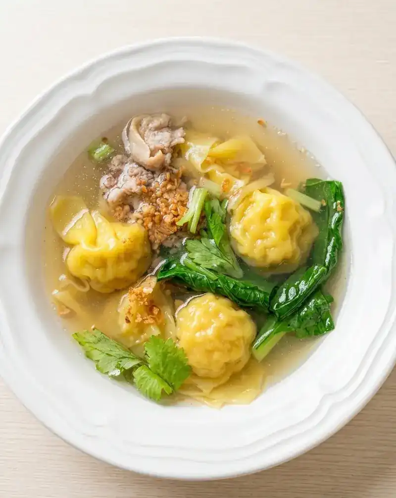 Wonton soup with greens in a white bowl