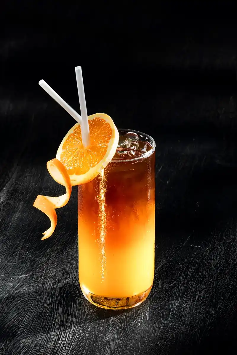 A tall glass of iced coffee layered with orange juice, with a slice of orange