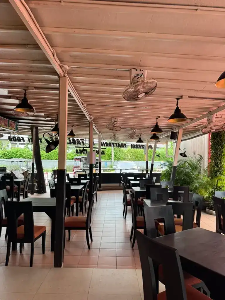 The open-air dining room under the terrace roof by day, dark wood tables and orange seats
