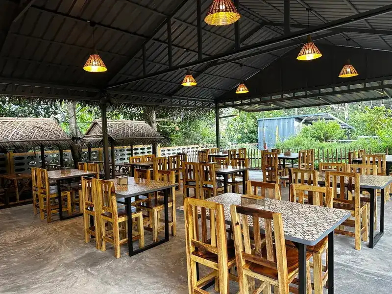 The open-sided dining room under rattan lamps, with wooden chairs and patterned tile tables